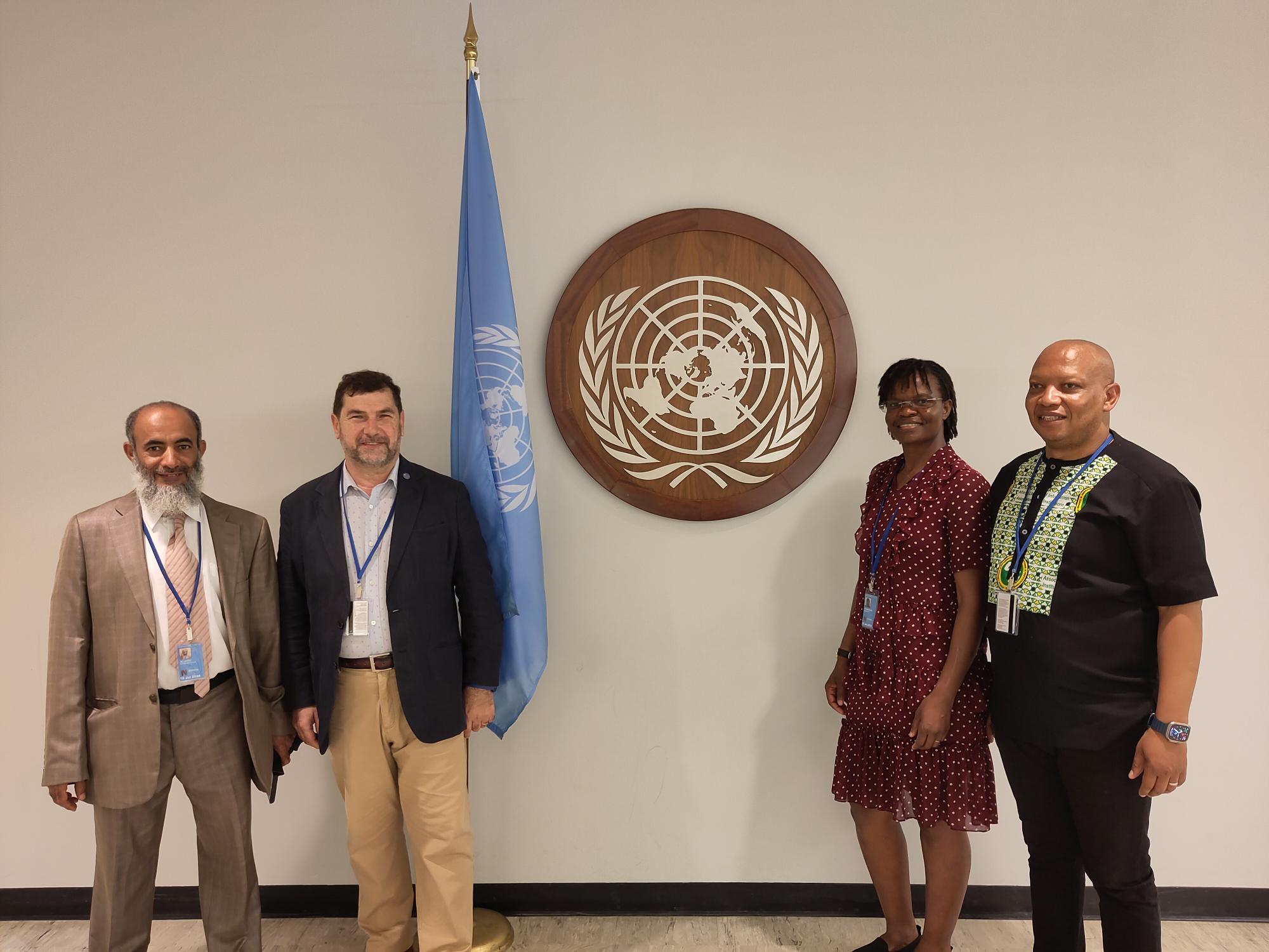 Four people in front of a UN logo and flag